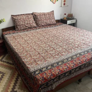 Red and indigo Kalamkari double bedsheet with bird and paisley border on a bed with two pillow covers