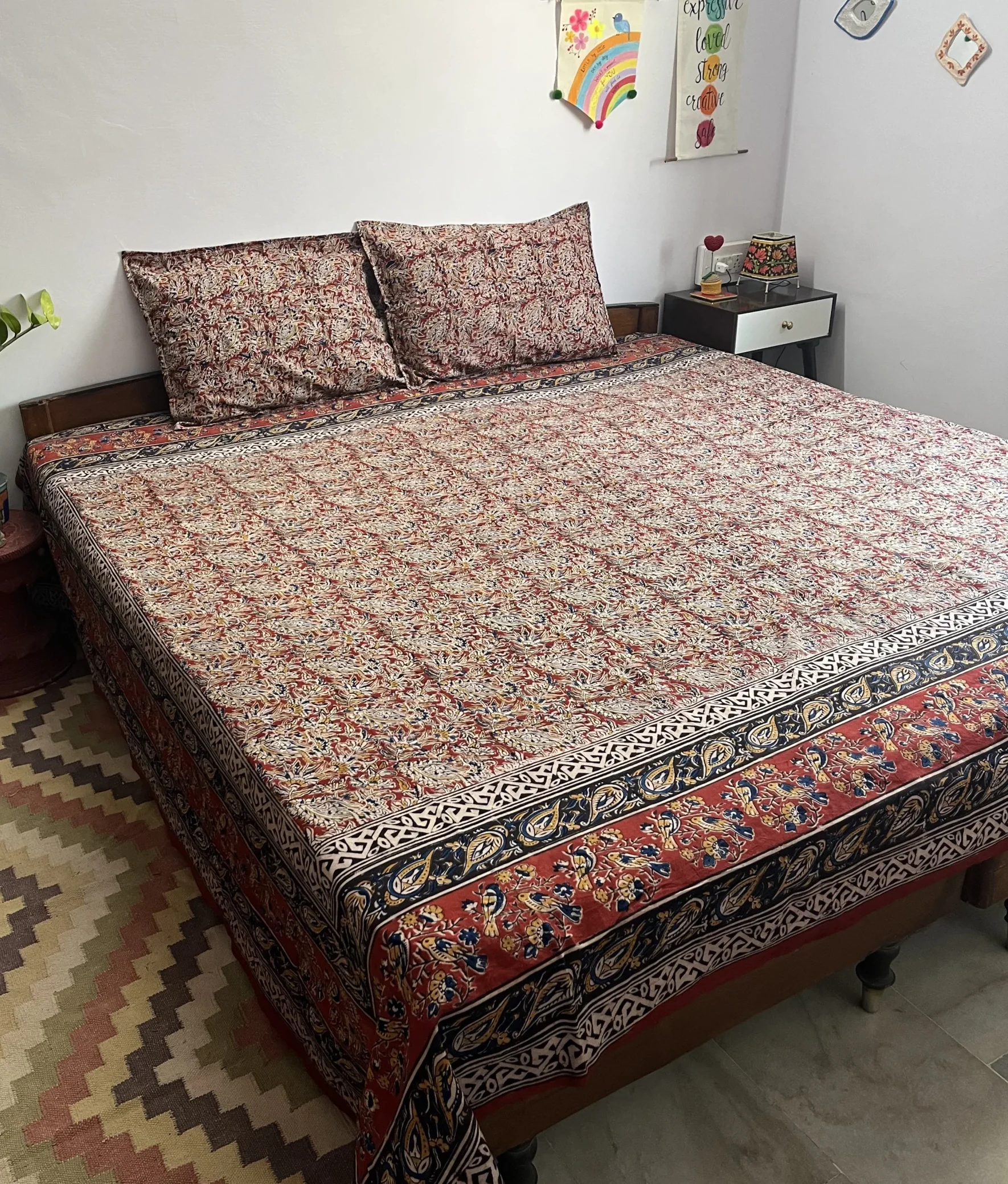 Red and indigo Kalamkari double bedsheet with bird and paisley border on a bed with two pillow covers