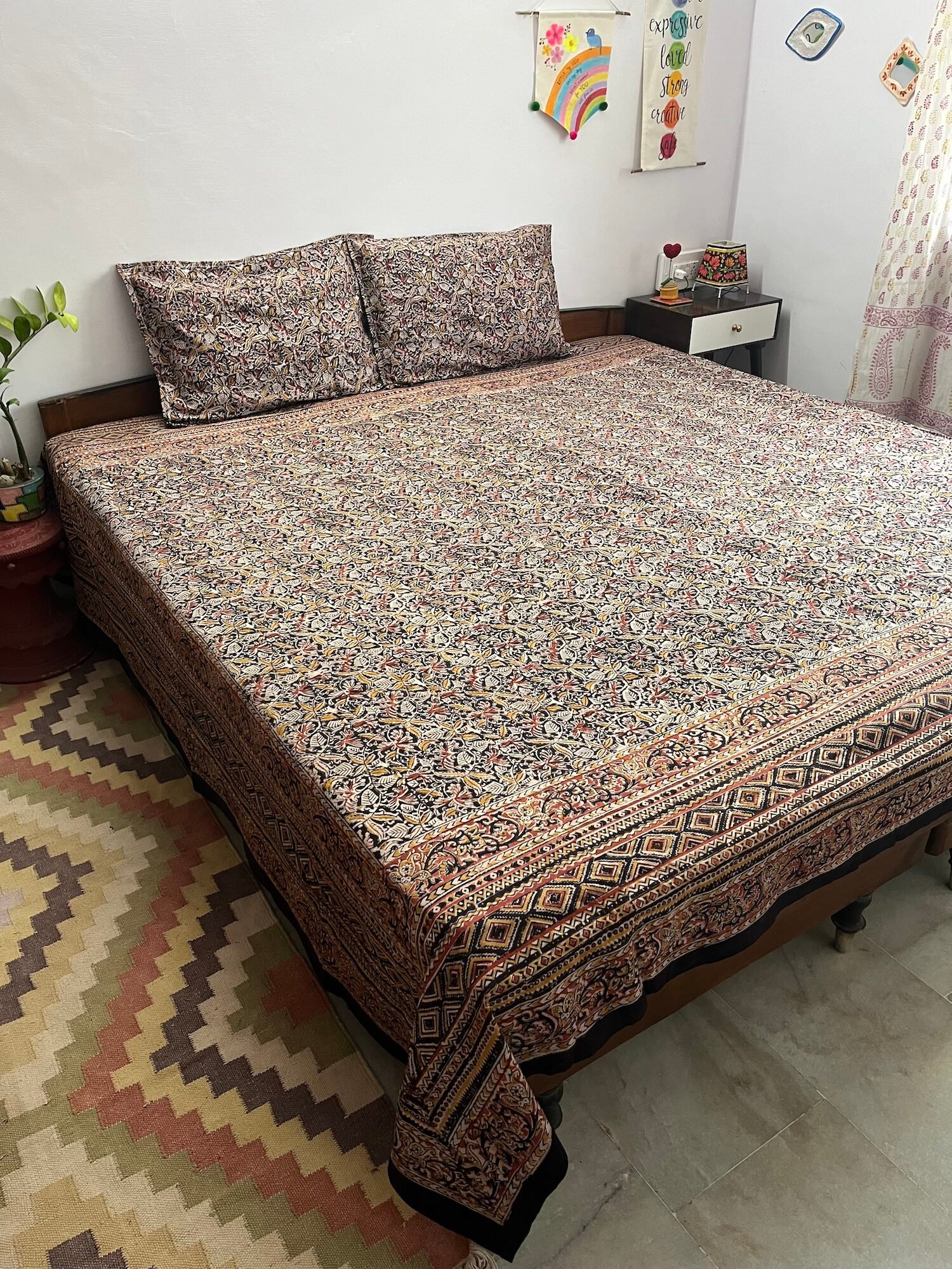Black and mustard Kalamkari double bedsheet with leaf print and diamond border on a bed with two pillow covers