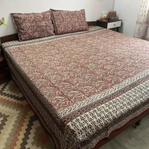 Madder red Kalamkari double bedsheet with leaf vine print and cream indigo border on a bed with two pillow covers