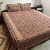 Coffee brown and mustard Kalamkari double bedsheet with floral creeper print and butterfly border on a bed with two pillow covers